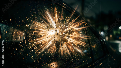 Car windshield with radial impact and water droplets during a night rainstorm