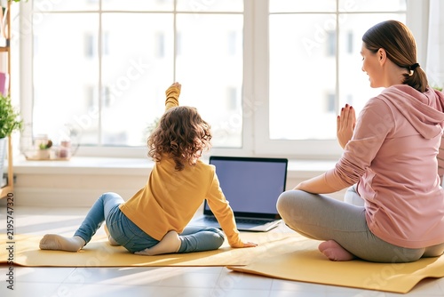 Happy mother and young child exercising on yoga mats at home while watching an online class on a laptop
