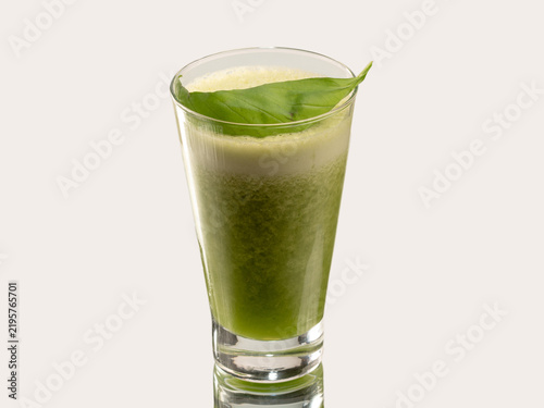 Tall glass of green smoothie garnished with a single basil leaf on the rim, shot on a light neutral background.