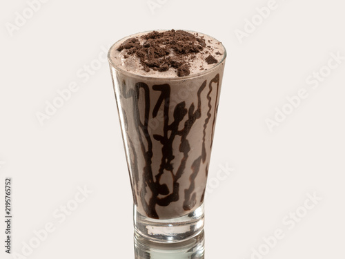 Tall glass of pale yellow coconut smoothie topped with coconut shavings, shot on a light neutral background.