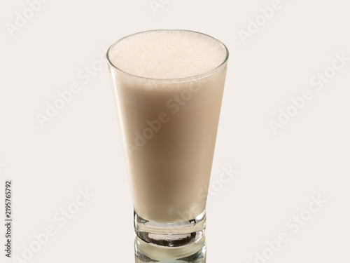 Tall glass of chocolate milkshake with chocolate drizzle and crushed cookie topping, shot on a light background.