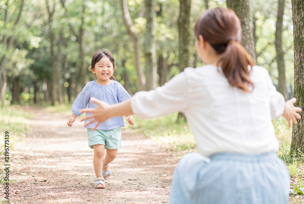Obraz premium Maman vue de dos, accroupie, bras ouverts, en chemise blanche et jupe bleu clair, accueillant sa petite fille asiatique souriante courant en haut rayé bleu et blanc, short vert pastel et sandales