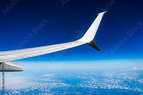 Passenger view of airplane wing and winglet flying above clouds in blue sky