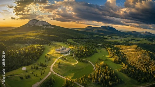 Drone shows a sweeping view of mountains and greenery during sunset with roads and structures visible below