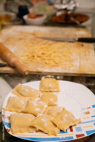 Homemade ravioli on plate with noodles in background