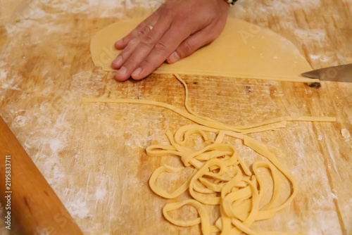 Slicing fresh pasta dough with knife on wooden board