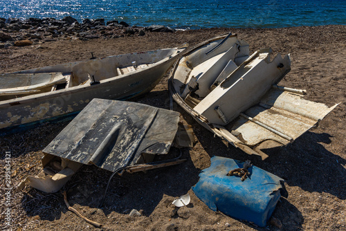Foto Small damaged fishing boat washed ashore and stranded on a sandy beach after being smashed against coastal rocks by the sea