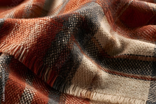 Detailed view of a folded plaid throw blanket featuring warm autumn colors and soft fringed edges
