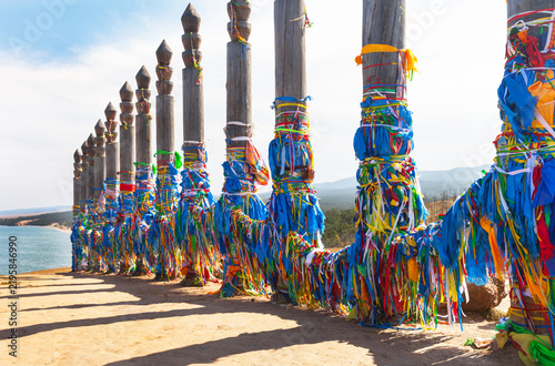 Baikal Lake. Olkhon Island. 13 Serge ritual pillars with blue and colorful ribbons and Hadaks of Buddhists and tourists near Khuzhir village. Tourist landmark of Cape Burkhan