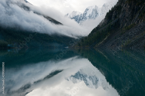 Early morning misty view of the Lower Shavlinskoye lake with mountain peaks named Dream, Fairy Tale and Beauty mirror themselves in the water, Russian Federation