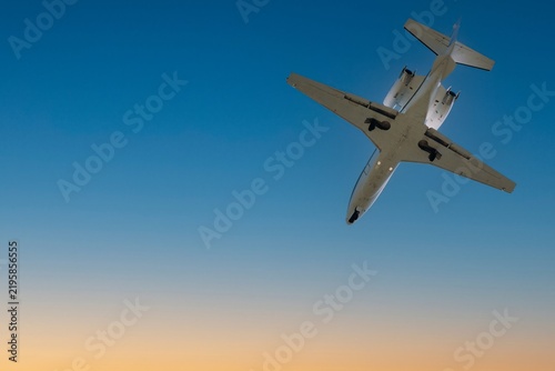 Business jet flying overhead with landing gear down against blue sky