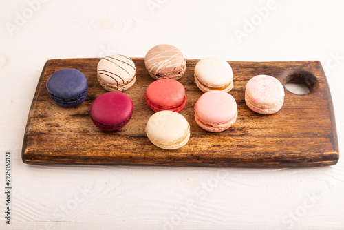 Macarons colourful cookies dessert on brown wooden cutting board on white wooden, side view, close up