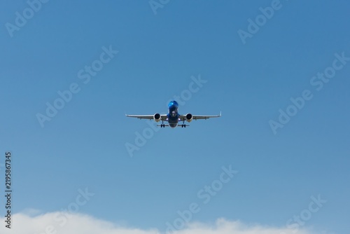 Passenger jet flying head-on with landing gear down in blue sky