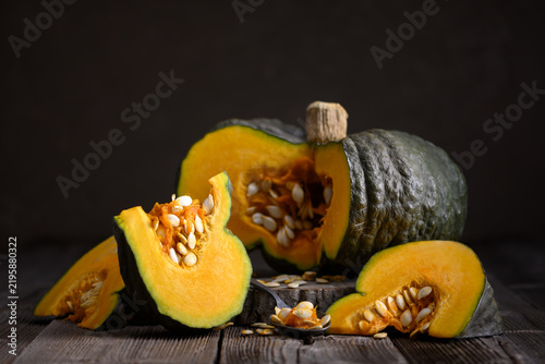Whole and sliced pumpkin arranged on rustic wooden table with scattered seeds. Autumn harvest still life with squash and seasonal cooking inspiration