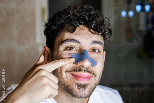 Young man applying a nose strip for skincare routine, focusing on self-care and grooming