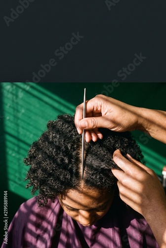Hairdresser parting curly afro textured hair with a metal styling tool during a salon grooming session