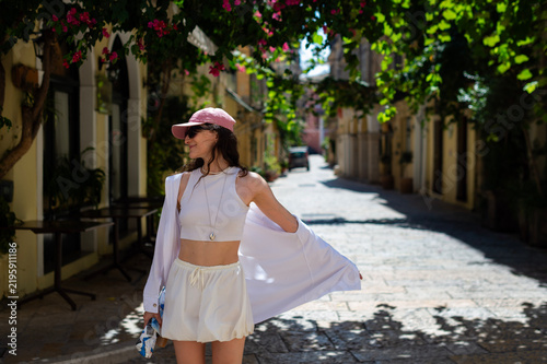 Foto A woman wearing a pink cap and white shorts outfit walks along a sunlit street in Kerkira, Greece