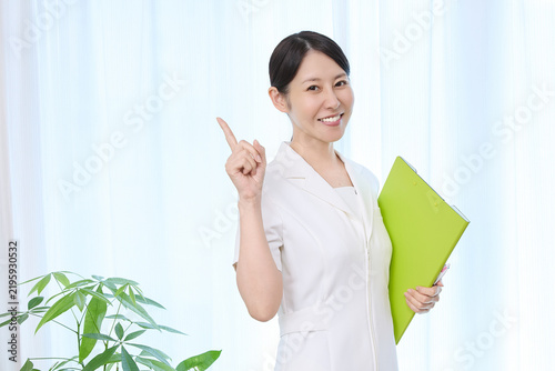 緑のファイルを抱え指を立てて案内する女性スタッフ