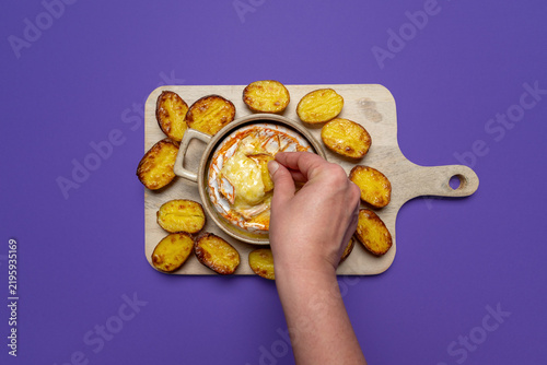 Hand dipping a potato into melted baked camembert