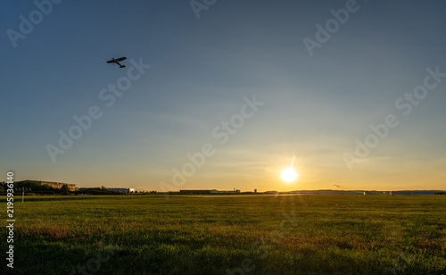 Small aircraft flying over an airfield at sunset