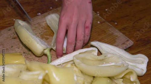 Preparing vegetables, a person uses a sharp knife to carefully slice fresh yellow bell peppers on a wooden board. Top-down static shot.