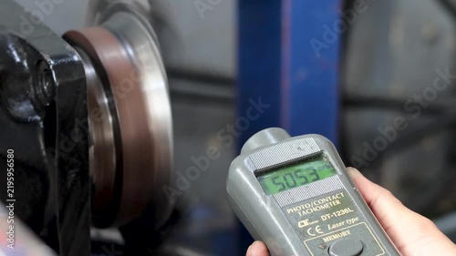 Technician measuring machinery rotating speed using digital photo tachometer inside workshop.