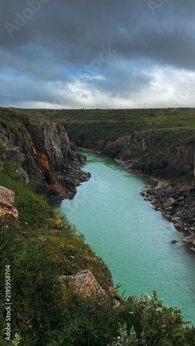 Turquoise river flowing through a dramatic Icelandic canyon surrounded by towering basalt cliffs and rugged volcanic scenery.
