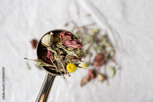 Close up of a spoonful of herbal tea on a natural linen tablecloth, rustic ingredient still life and organic wellness concept