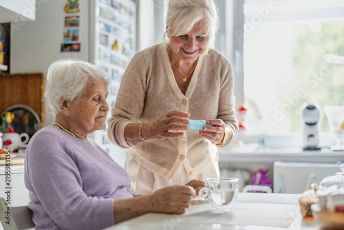 Caregiver giving elderly woman medicine in kitchen

