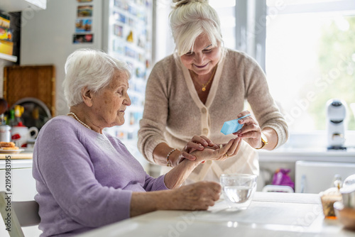 Caregiver giving elderly woman medicine in kitchen
