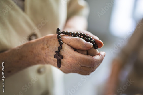 Elderly woman praying with rosary beads in her hands
