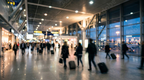 Blurred travelers walking through busy airport terminal carrying luggage during evening with soft ambient interior lighting