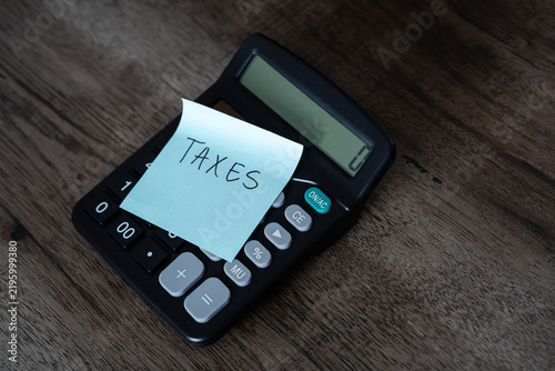 Фотография Blue sticky note with taxes text stuck on black calculator on wooden desk