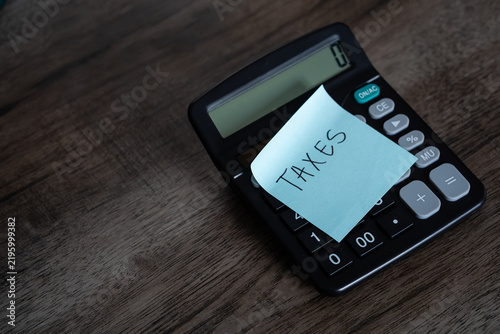 Foto Blue sticky note with taxes text stuck on black calculator on wooden desk