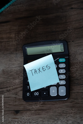 Obraz na plátne Blue sticky note with taxes text stuck on black calculator on wooden desk