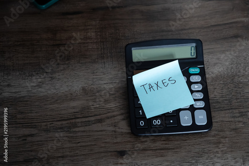 Fotografie Blue sticky note with taxes text stuck on black calculator on wooden desk