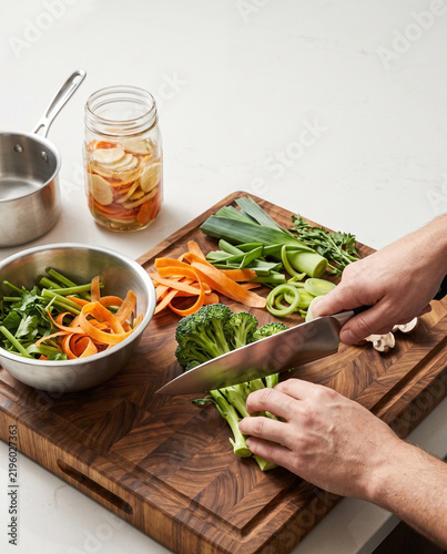 Person chopping fresh broccoli with knife on wooden cutting board in kitchen