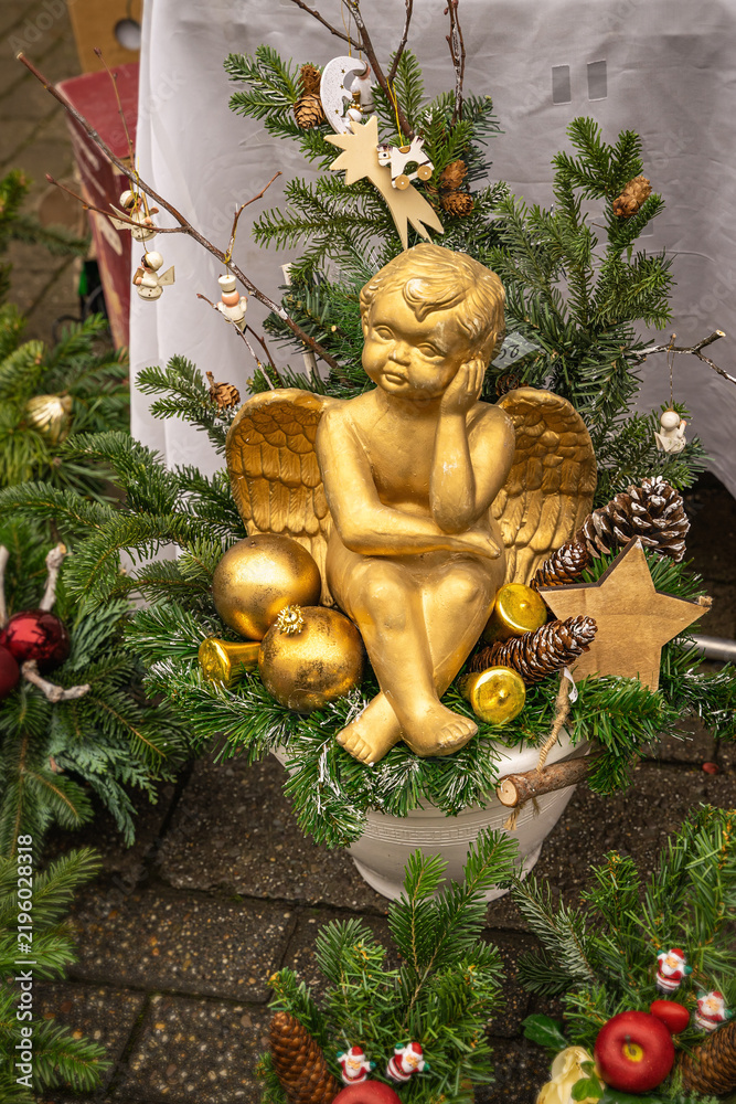 Fototapeta premium Gold Christmas Angel Decoration. Gold angel figurine surrounded by evergreen branches, Christmas ornaments, pine cones, wooden star. Christmas angel arrangement, traditional festive holiday decoration