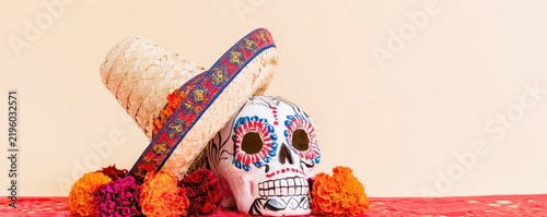 Decorated sugar skull wearing a straw sombrero surrounded by colorful marigold flowers