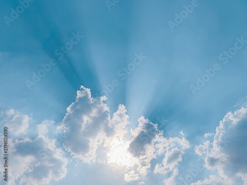 Radiant sunlight bursting behind majestic cumulus clouds spreading dramatic light rays across a bright turquoise sky.