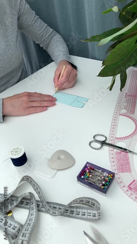 Vertical video. A beginner seamstress, tailor draws lines on a skirt mock‑up; the lady works with a pattern and sewing tools. Mastering sewing skills from scratch, practical training
