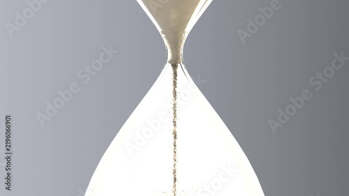 Emptying top bulb clear hourglass releasing tan sand into lower bulb forming conical pile in studio