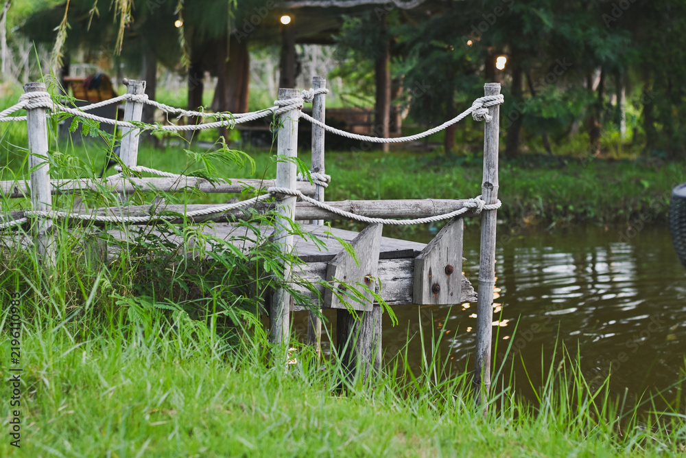 Naklejka premium Wooden pier with rope railing beside a pond in park.
