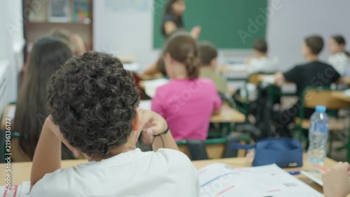 Students sitting at desks in a classroom while listening to a teacher during a school lesson