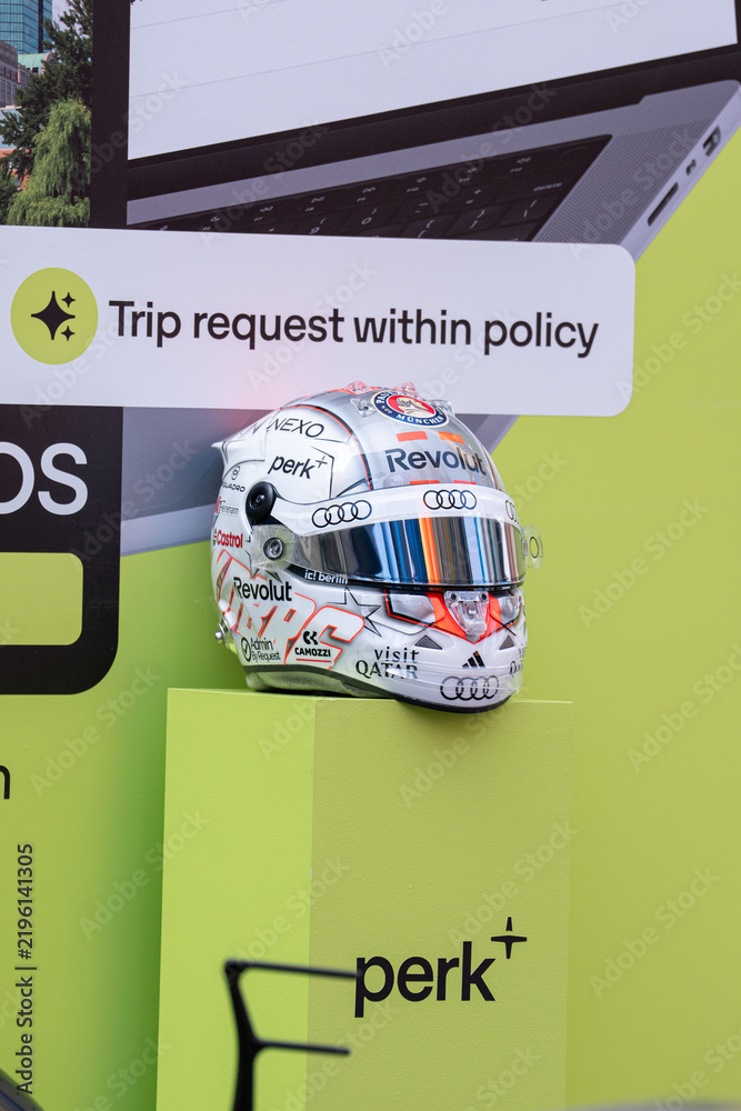 Obraz premium NEW YORK, USA – SEPTEMBER 16, 2026: a Formula One racing helmet display with sponsor logos on a bright green promotional backdrop.