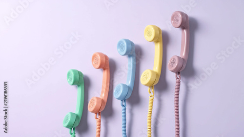 Colorful vintage telephone handsets arranged diagonally on a lilac background