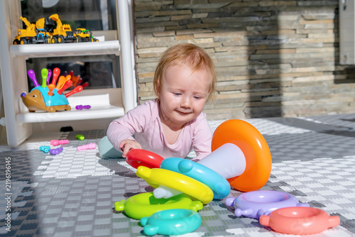 Cute adorable baby child girl playing pyramid toy at home,lying on stomach.toddler building tower of rings.Children logic development,early sensory education,happy childhood