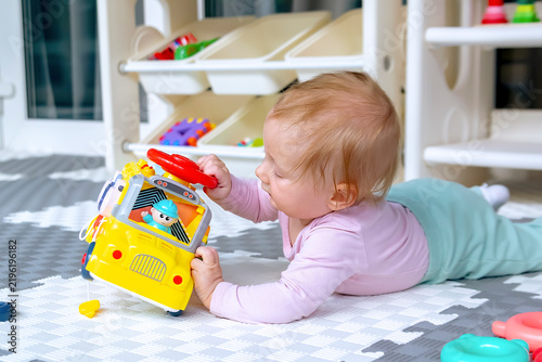 Cute little baby lying on stomach,girl playing at home with car toy,exploring in playing room.Children logic development,early sensory education,happy childhood