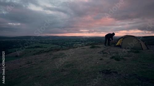 A man setting up his wild camping tent at dusk in the hills of England