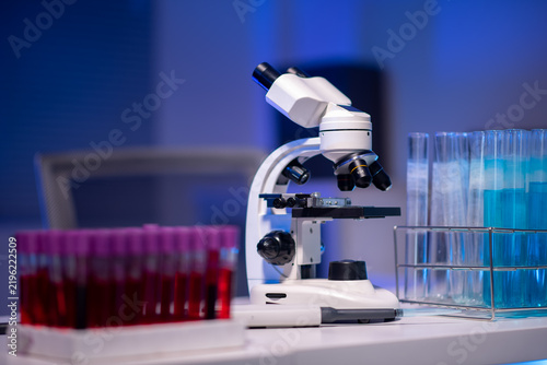 Foto Professional laboratory microscope with blood sample test tubes and blue liquid